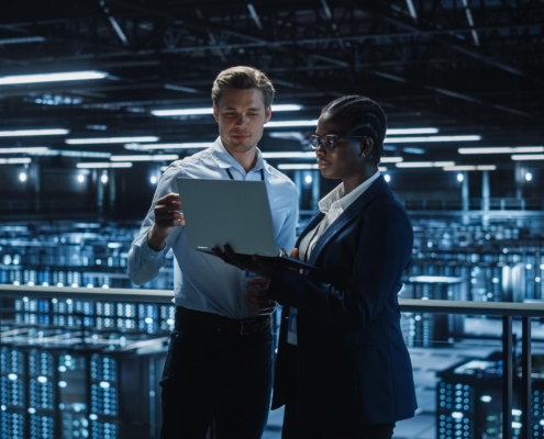 Image of two people looking at a laptop inside of a data center.