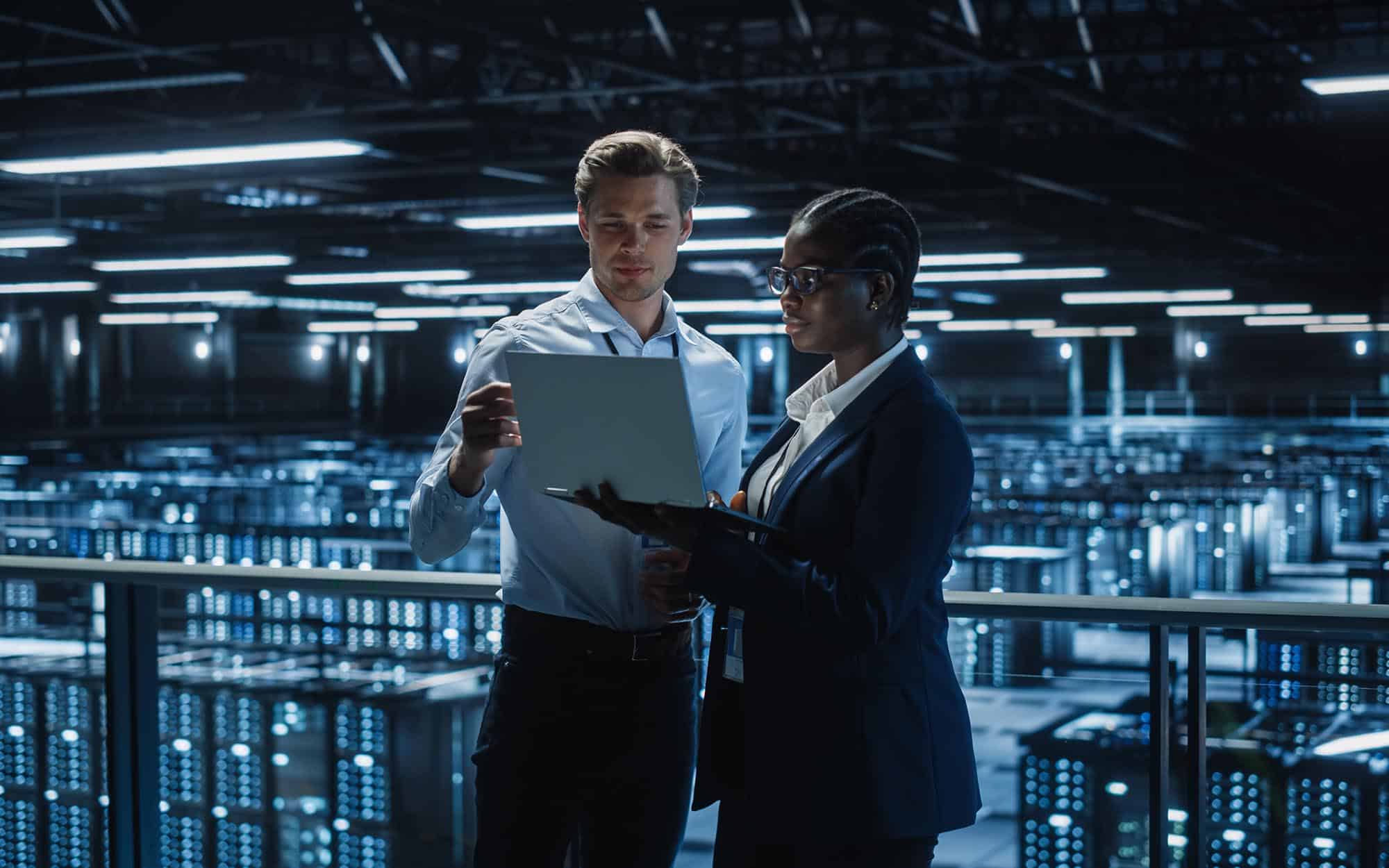 Image of two people looking at a laptop inside of a data center.