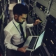 Image of a business person in a server room, looking at a laptop.