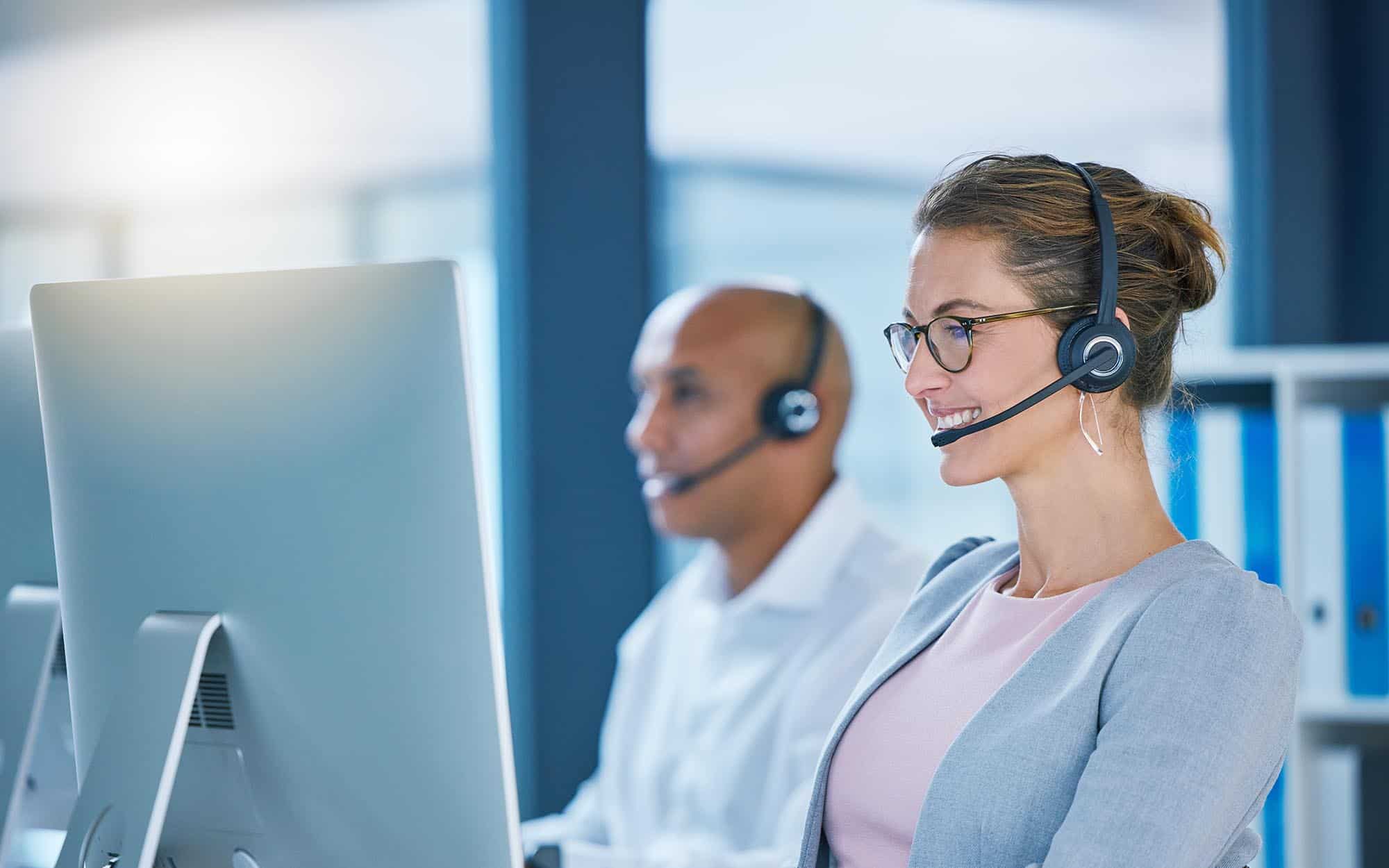 Side view of two IT professionals on computers while wearing headsets